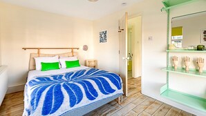 Une chambre à coucher comprenant un lit, une table de chevet, une commode, une étagère verte ornée d’objets décoratifs et une porte donnant sur une autre pièce.