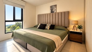 A modern bedroom with a large bed, a headboard, a nightstand with a lamp, and a view of the outdoors. - Maravilia 3 bedrooms/2 bathrooms/2 (Guadalajara)