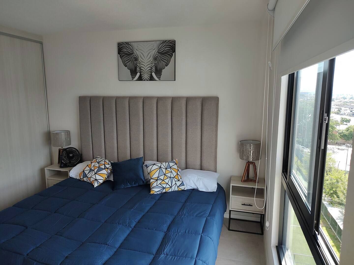 Une chambre à coucher avec un lit, une table de chevet, une lampe et une fenêtre donnant sur la ville.