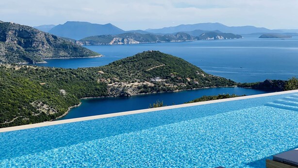 Ein klares, blaues Infinity-Pool mit Blick auf eine Küstenlandschaft, einschließlich einer kleinen Insel und ferner Berge.