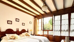 Une chambre à coucher avec un lit double, une tête de lit en bois, une table de chevet, une lampe, une fenêtre avec des rideaux et un plancher carrelé.
