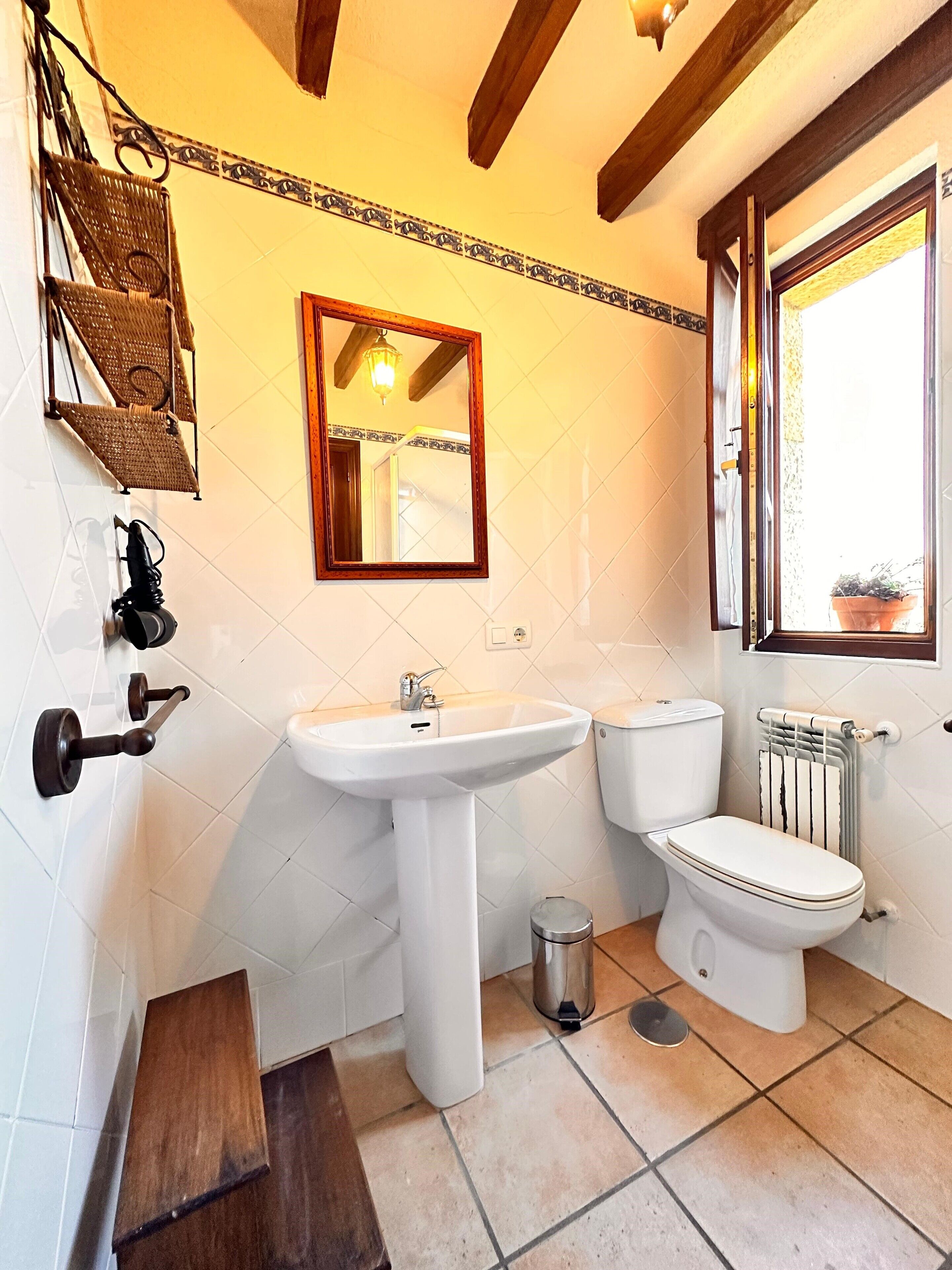 A bathroom with a white sink, toilet, and a mirror above the sink. There is a window on the right side and a radiator below it.