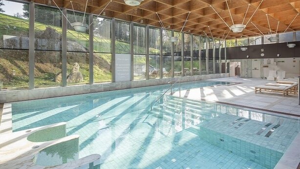 Une piscine intérieure avec des parois en verre transparent, un plafond en bois et un sol carrelé.