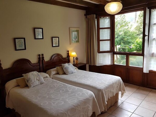 Una habitación con dos camas, techo de madera, cuadros enmarcados en la pared, una ventana con cortinas y una lámpara sobre una mesita de noche.