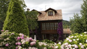 Un chalet traditionnel avec un toit en tuiles, entouré d’une végétation luxuriante et de plantes en fleurs.