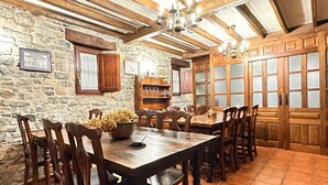 Un espace repas comprenant une grande table en bois, des chaises, un lustre, des murs en pierre et des portes en bois.