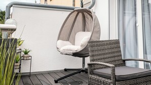 A balcony with a wicker chair and a hanging chair, a potted plant, and a building in the background. - Fantastic apartment - Terrace- Hanging chair- Highspeed WiFi (Viersen)