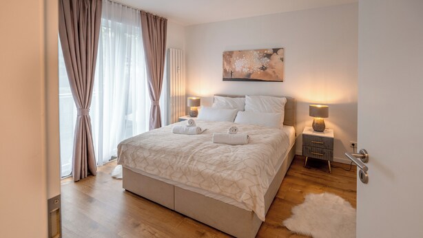 A modern bedroom with a large bed, two bedside tables with lamps, a fluffy rug, and a painting on the wall. - Fantastic apartment - Terrace- Hanging chair- Highspeed WiFi (Viersen)