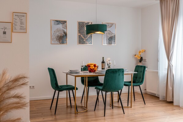 A dining area with a round table, four green chairs, a green pendant light, and framed artwork on the wall. - Fantastic apartment - Terrace- Hanging chair- Highspeed WiFi (Viersen)