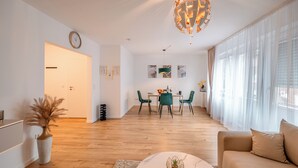 A modern living room with a wooden floor, a round marble coffee table, a beige sofa, and a dining area with green chairs and a table. - Fantastic apartment - Terrace- Hanging chair- Highspeed WiFi (Viersen)