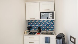 A compact kitchenette with white cabinets, a microwave, a sink, and a patterned backsplash. - YourHome - Casa Lucente (Positano)