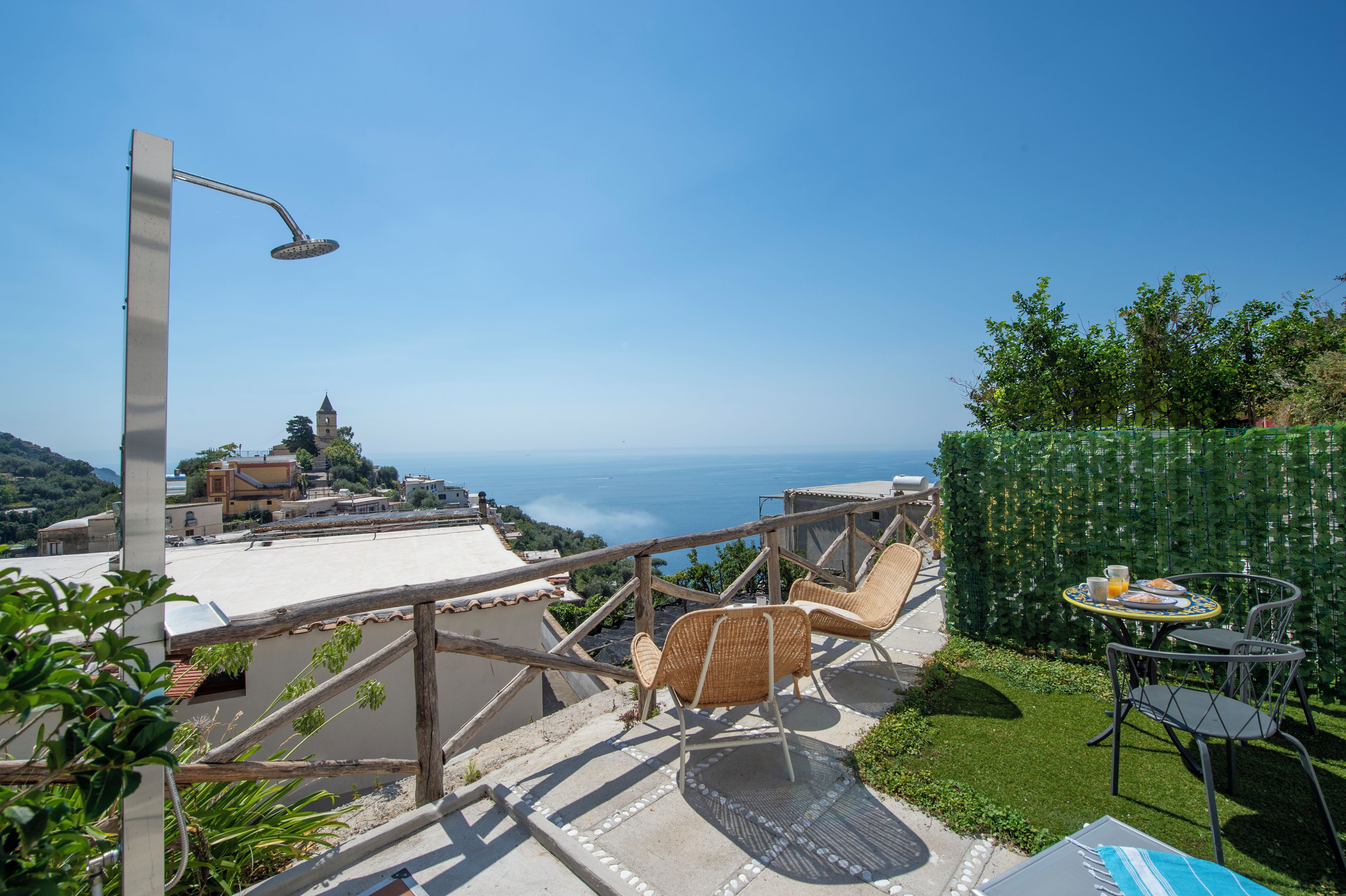 Une terrasse avec des sièges extérieurs, une vue sur la mer et une église visible au loin.
