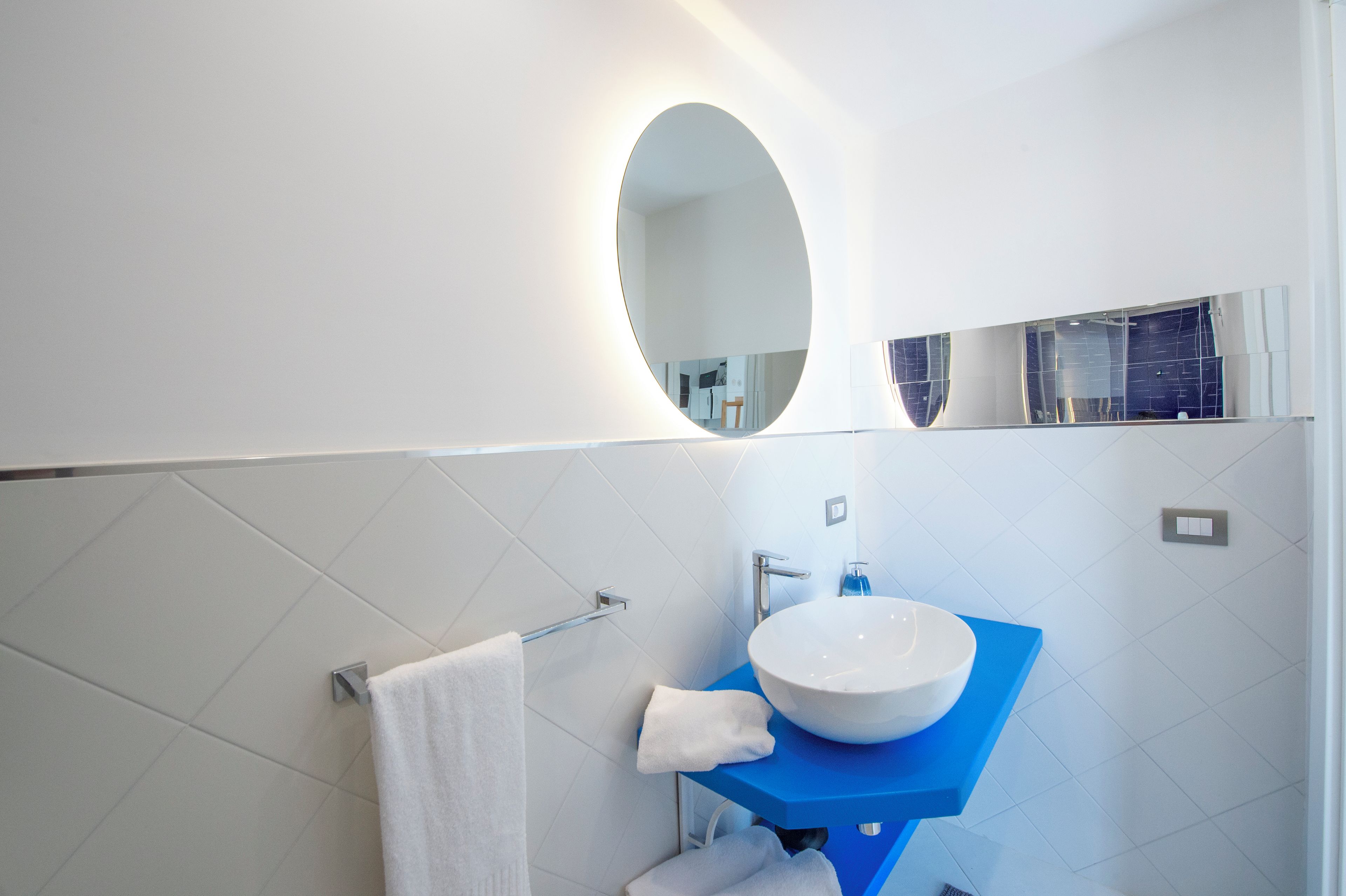 A modern bathroom with a white sink, blue countertop, and a large mirror.