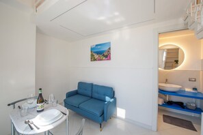 Ein modernes Badezimmer mit einem blauen Sofa, einem runden Spiegel und einem Gemälde einer Küstenlandschaft.