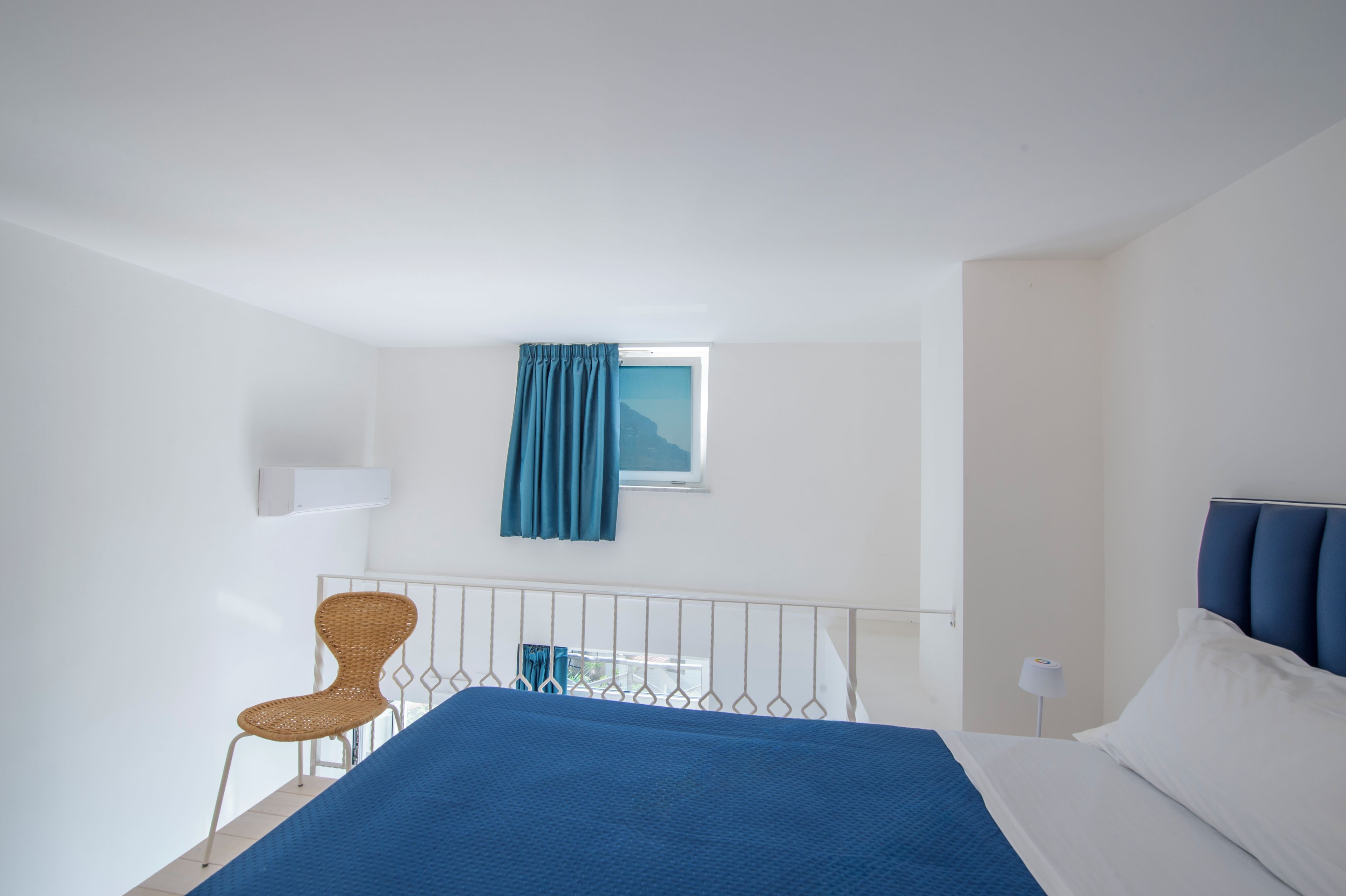 Ein Hotelzimmer mit einem Bett, einem Sessel, einem Fenster mit Vorhängen und einer Wand-Klimaanlage.