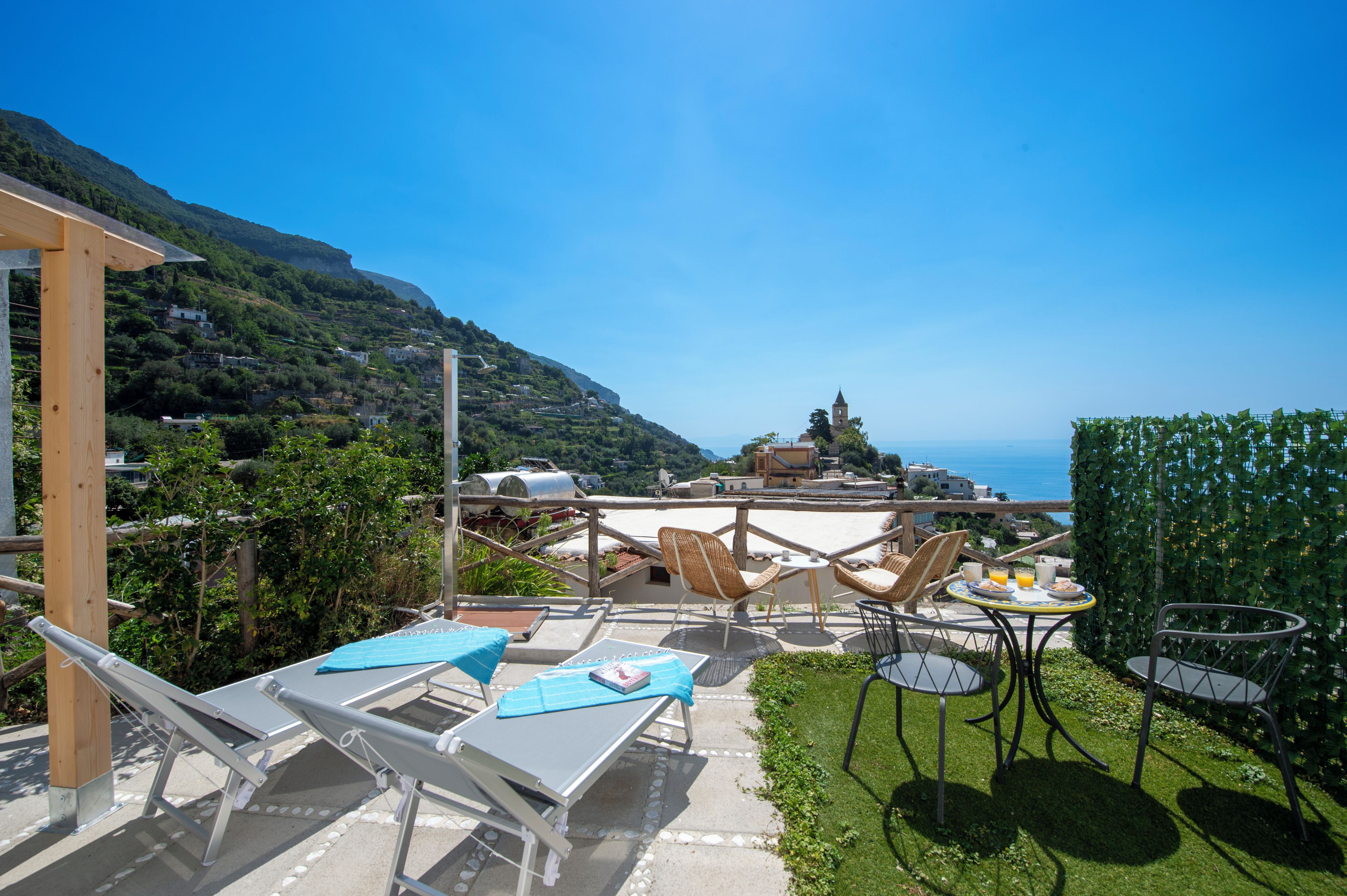 A terrace with outdoor seating, a view of the sea, and a mountain backdrop.
