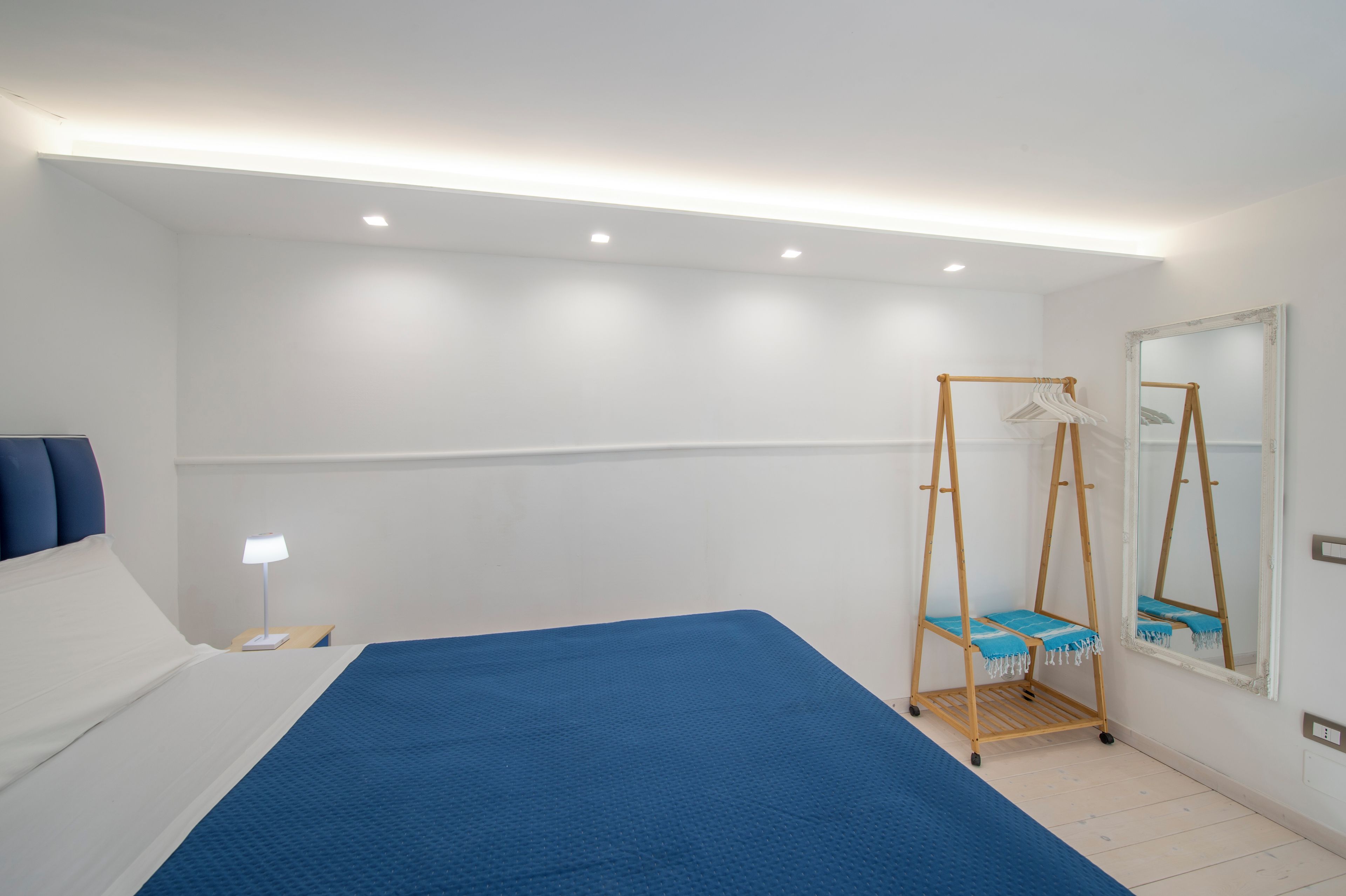 A hotel room with a bed, bedside table, lamp, and a wooden swing chair with a blue cushion.