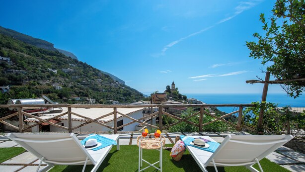 A terrace with two sun loungers, a small table with a basket, and a view of the sea and a church on a hillside. - YourHome - Casa Lucente (Positano)