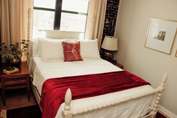 A neatly made bed with a red throw blanket, a bedside lamp, and a framed picture on the wall.