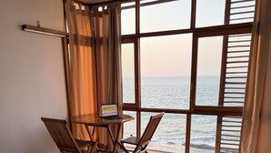 Une chambre dotée d’un grand lit, d’un bureau avec un ordinateur portable, de deux chaises et offrant une vue sur la mer grâce à de grandes fenêtres.