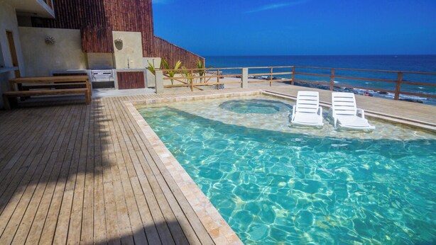 Une terrasse en bois avec une piscine, des chaises longues et une vue sur l’océan.
