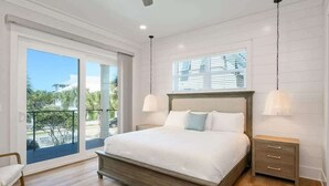 Un dormitorio con una cama grande, una mesita de noche, una ventana con persianas y un balcón con vistas.