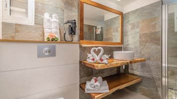 A modern bathroom with a marble wall, a wooden vanity, a sink, and a shower area.
