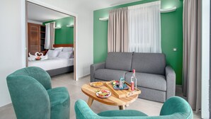 A modern hotel room with a grey sofa, a wooden coffee table with breakfast items, and a green wall. - Hôtel Le Courbaril (Trois-Ilets)