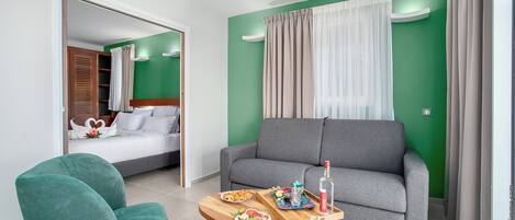 A modern hotel room with a grey sofa, a wooden coffee table with breakfast items, and a green wall.