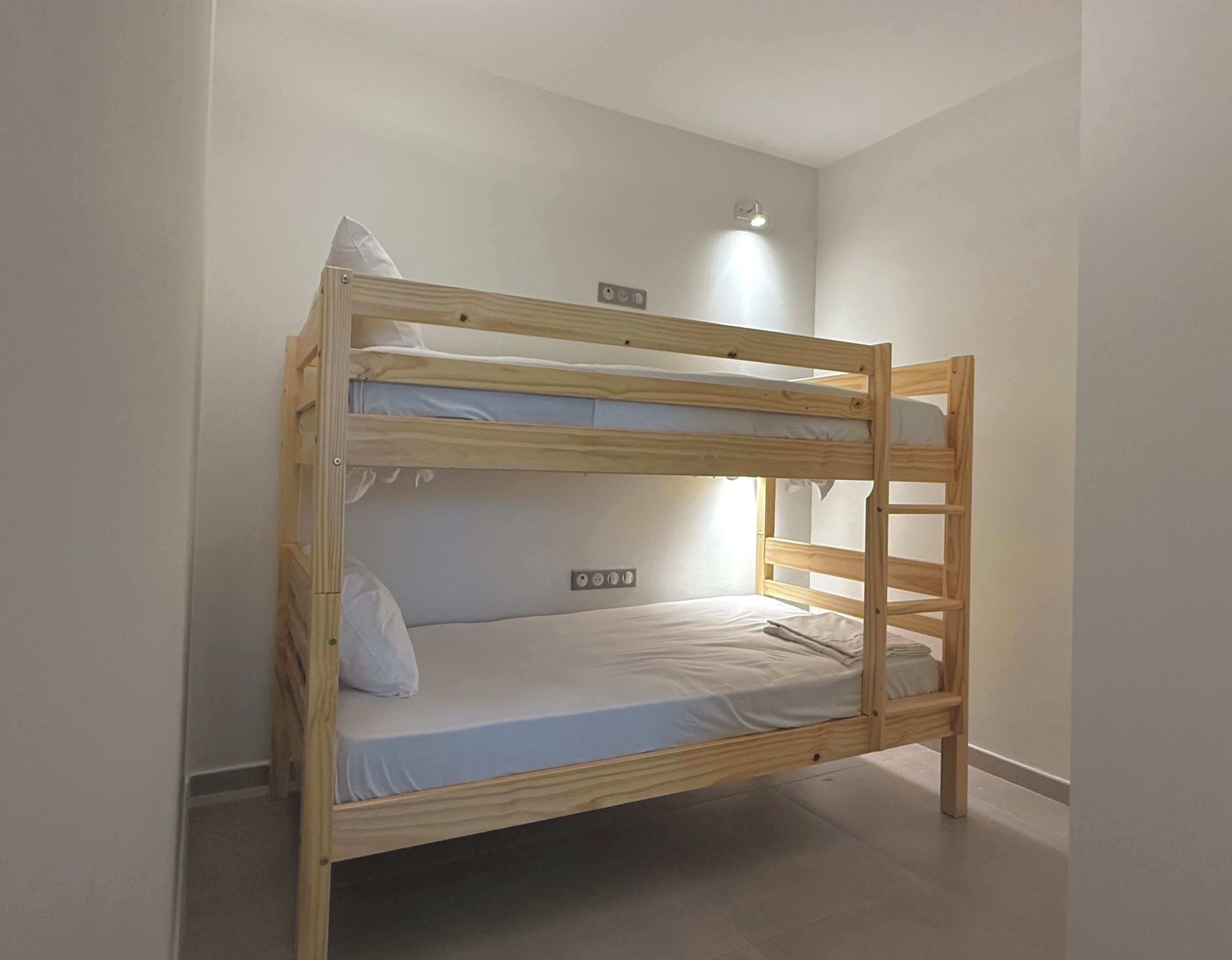 Un lit superposé avec une échelle, une prise de courant et une applique murale.