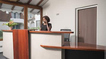 A reception desk with a wooden finish, a potted plant, and a view of a balcony with a railing.