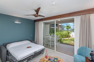 Una camera da letto con un letto, una ventola a soffitto, una porta scorrevole in vetro che dà su un balcone e un tavolino con una bottiglia e dei bicchieri.