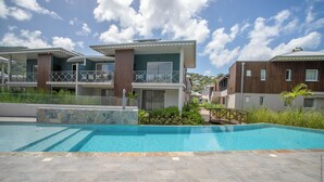 A modern residential complex with a swimming pool, multiple balconies, and a stone facade. - Hôtel Le Courbaril (Trois-Ilets)