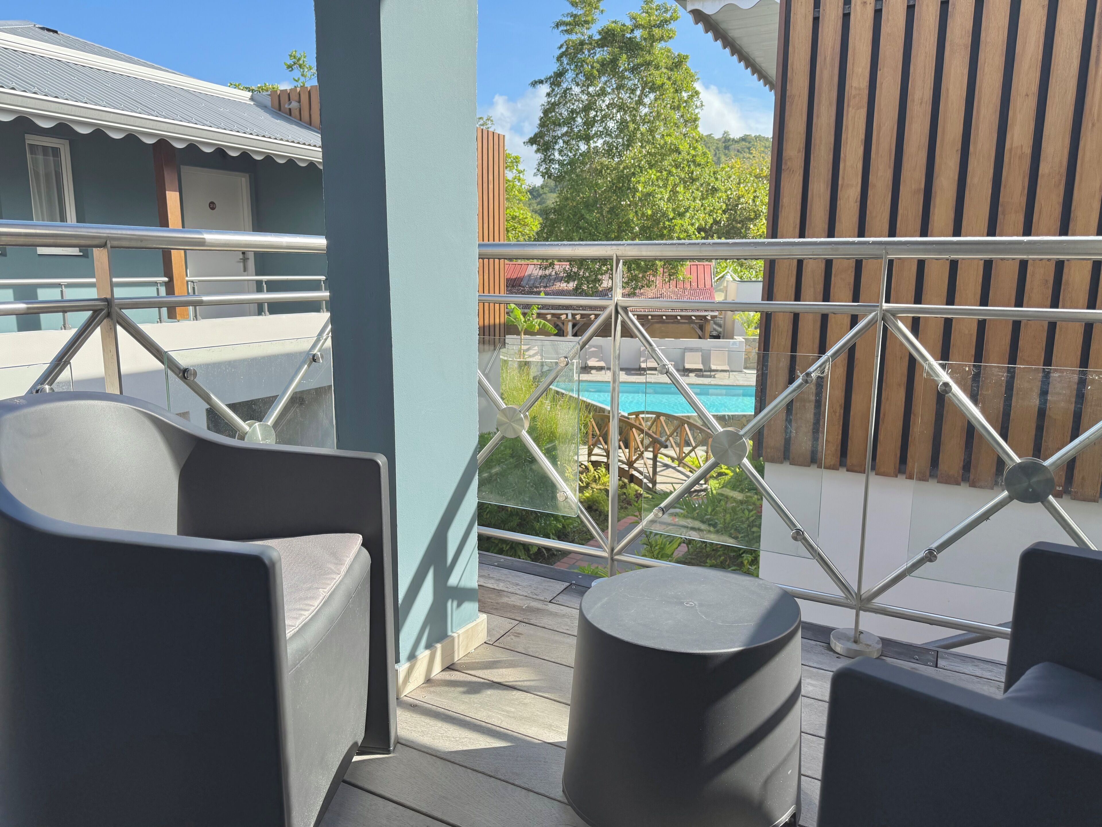 A balcony with two chairs and a small table, overlooking a swimming pool and a wooden fence.