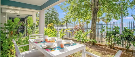An outdoor dining area with a table set for two, surrounded by lush greenery and a view of the sea.