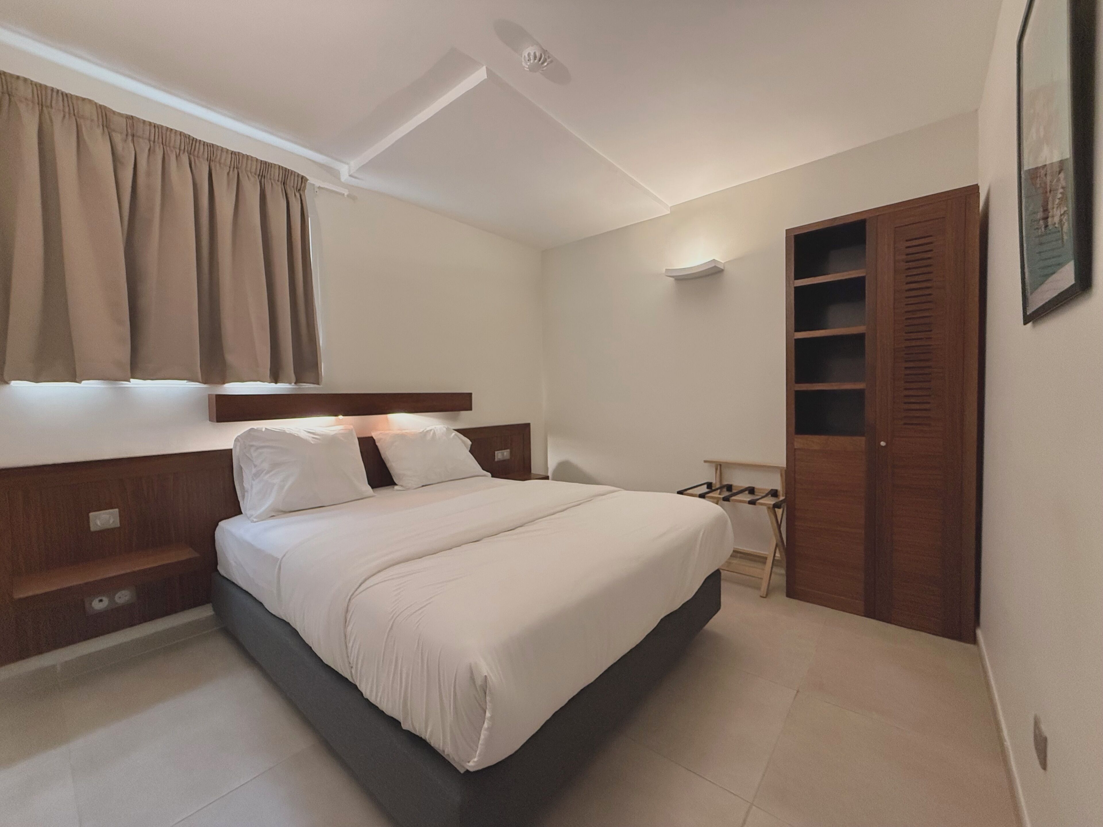 Ein Schlafzimmer mit einem Bett, einem Kleiderschrank, einem Nachttisch und einem Fenster mit Vorhängen.