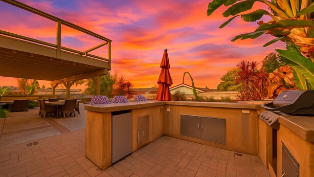 Une terrasse extérieure équipée d’un barbecue, d’un espace salon et offrant une vue sur le coucher de soleil.
