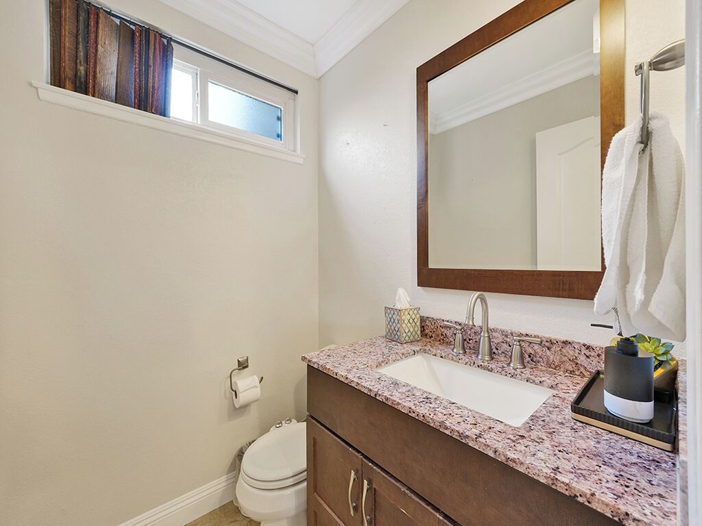 Un baño con inodoro blanco, lavabo con encimera de mármol, espejo grande y toallero.