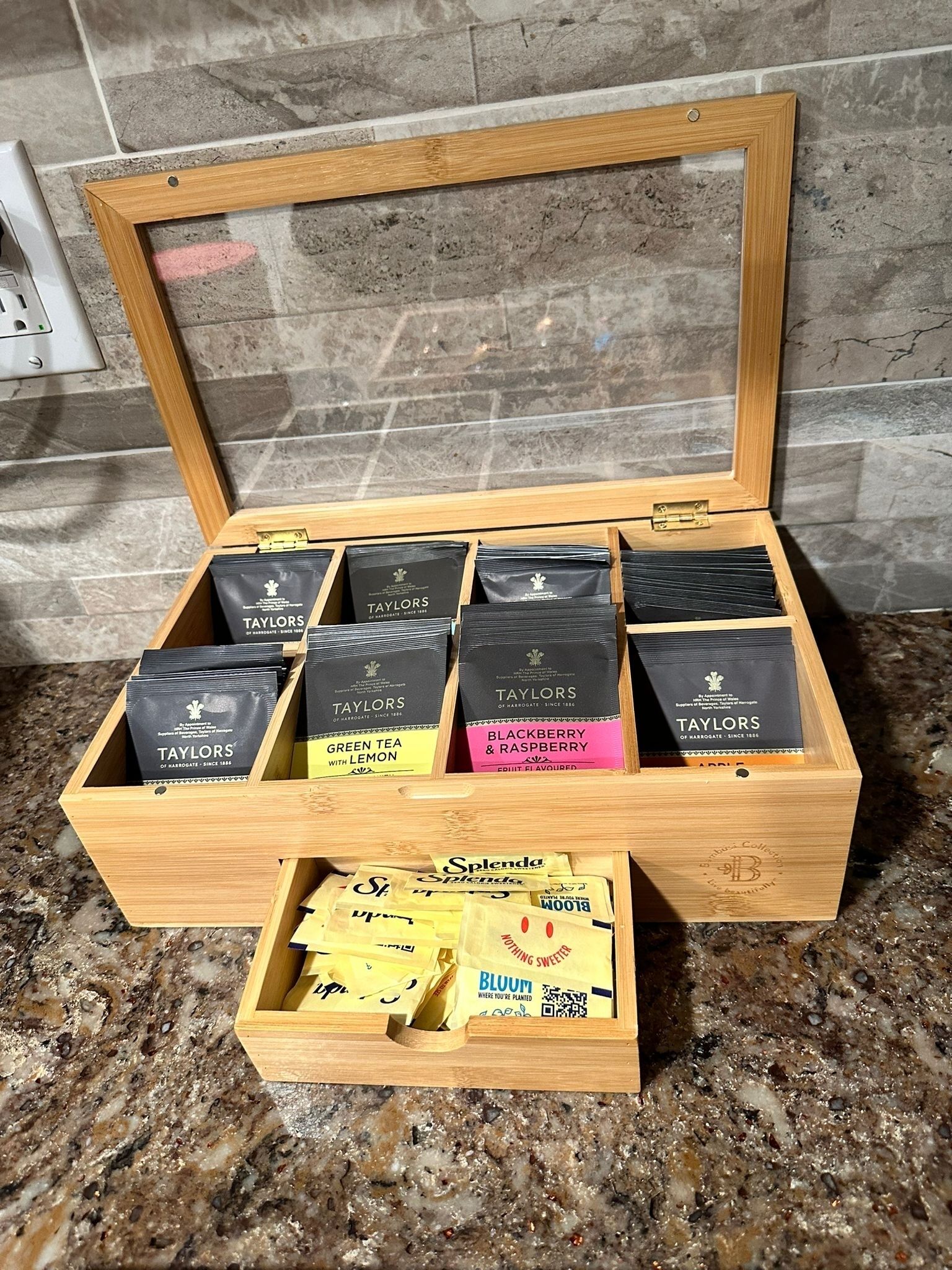 A wooden box with compartments containing various tea packets, including brands like Taylors and Splenda.