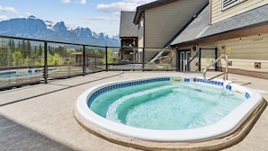 A hot tub with a mountain view, a wooden building, and a glass railing. - Rundle Cliffs Lodge by Canmore Premier  (Canmore)