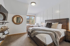 A bedroom with a large bed, a TV, a mirror, and a window with blinds. - Rundle Cliffs Lodge by Canmore Premier  (Canmore)