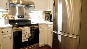Una cocina con electrodomésticos de acero inoxidable, armarios blancos y un letrero en pizarra.