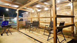 Un patio al aire libre con mesas y sillas de madera, una parrilla y un muro de ladrillo.