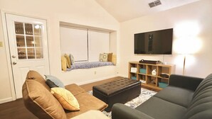 Una sala de estar con un sofá, un reposapiés y un televisor montado en la pared.