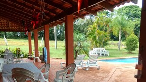 A covered outdoor area with tables and chairs, a brick floor, and a view of a swimming pool and greenery. - Marisol, spacious and comfortable farm in Araçoiaba da Serra  (Araçoiaba da Serra)