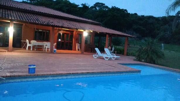 A pool area with lounge chairs, a covered patio, and a building with a tiled roof. - Marisol, spacious and comfortable farm in Araçoiaba da Serra  (Araçoiaba da Serra)