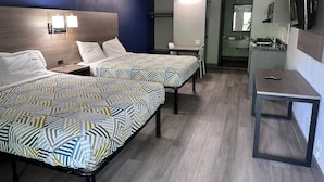 Ein Hotelzimmer mit zwei Betten, einem Schreibtisch, einem Sessel, einem Fernseher und einem durchgegangenen Tür sichtbaren Badezimmer.
