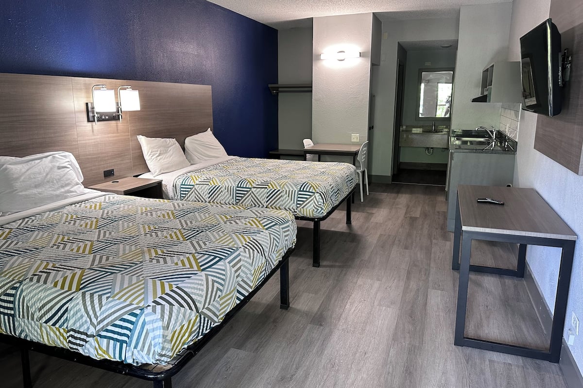 A hotel room with two beds, a desk, a chair, a TV, and a bathroom visible through an open door.