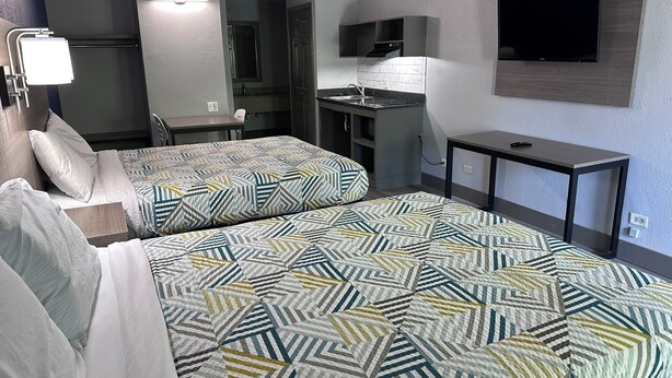 Ein Hotelzimmer mit zwei Betten, einer Küchenzeile, einem Fernseher und einem Schreibtisch.
