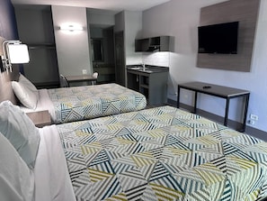A hotel room with two beds, a kitchenette, a TV, and a desk. - Studio Suites Extended Stay  (Chattanooga)